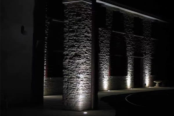 A focused beam of light from an LED wall washer grazing a textured building facade at night